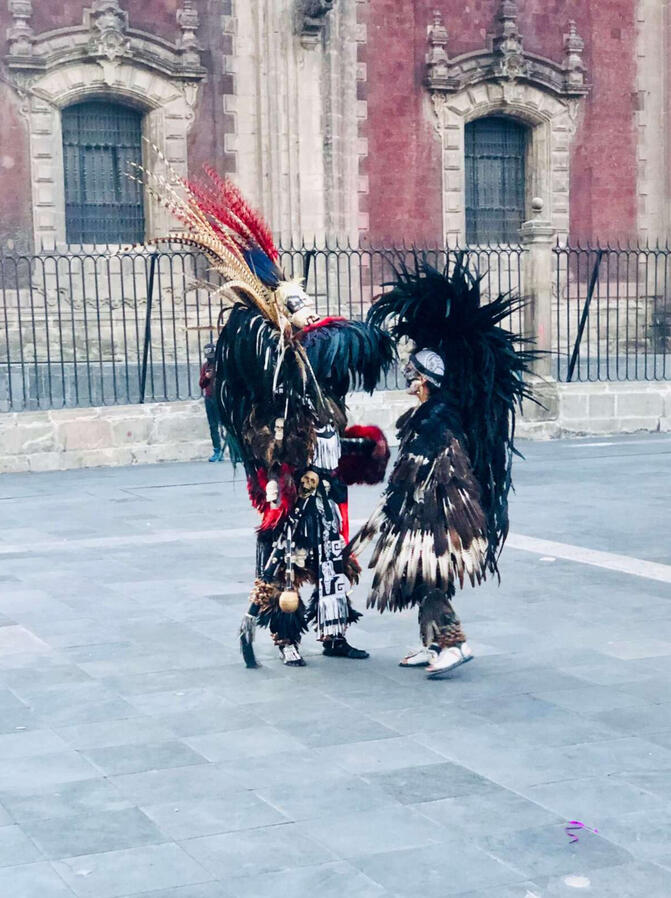 Dancers in traditional Aztec ceremonial attire performing in Mexico City's Zocalo square during a cultural walking tour