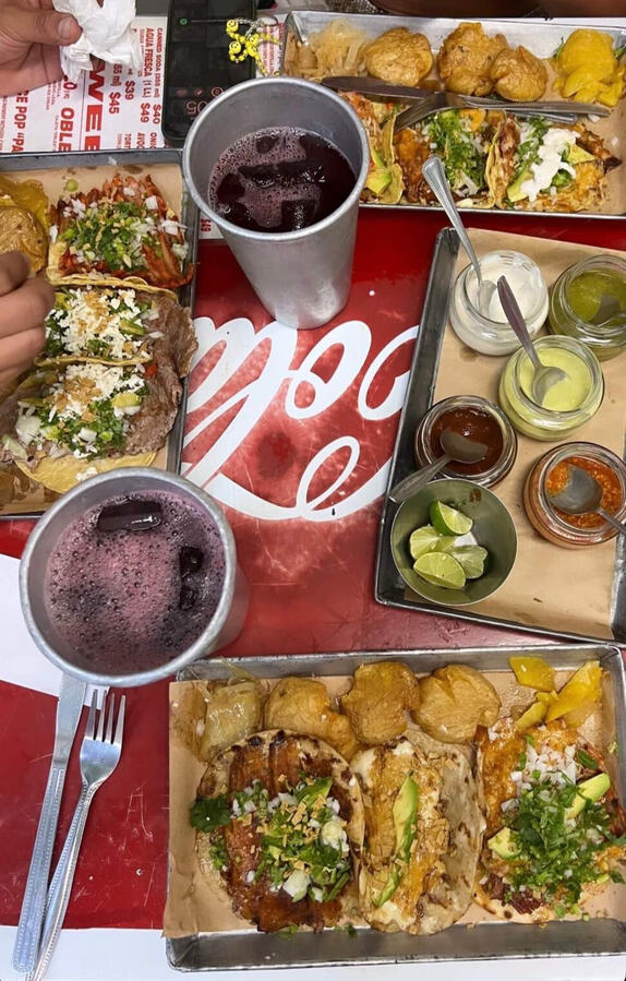 vibrant table set with various tacos on metal trays, salsas, and hibiscus water at Taqueria Orinoco,