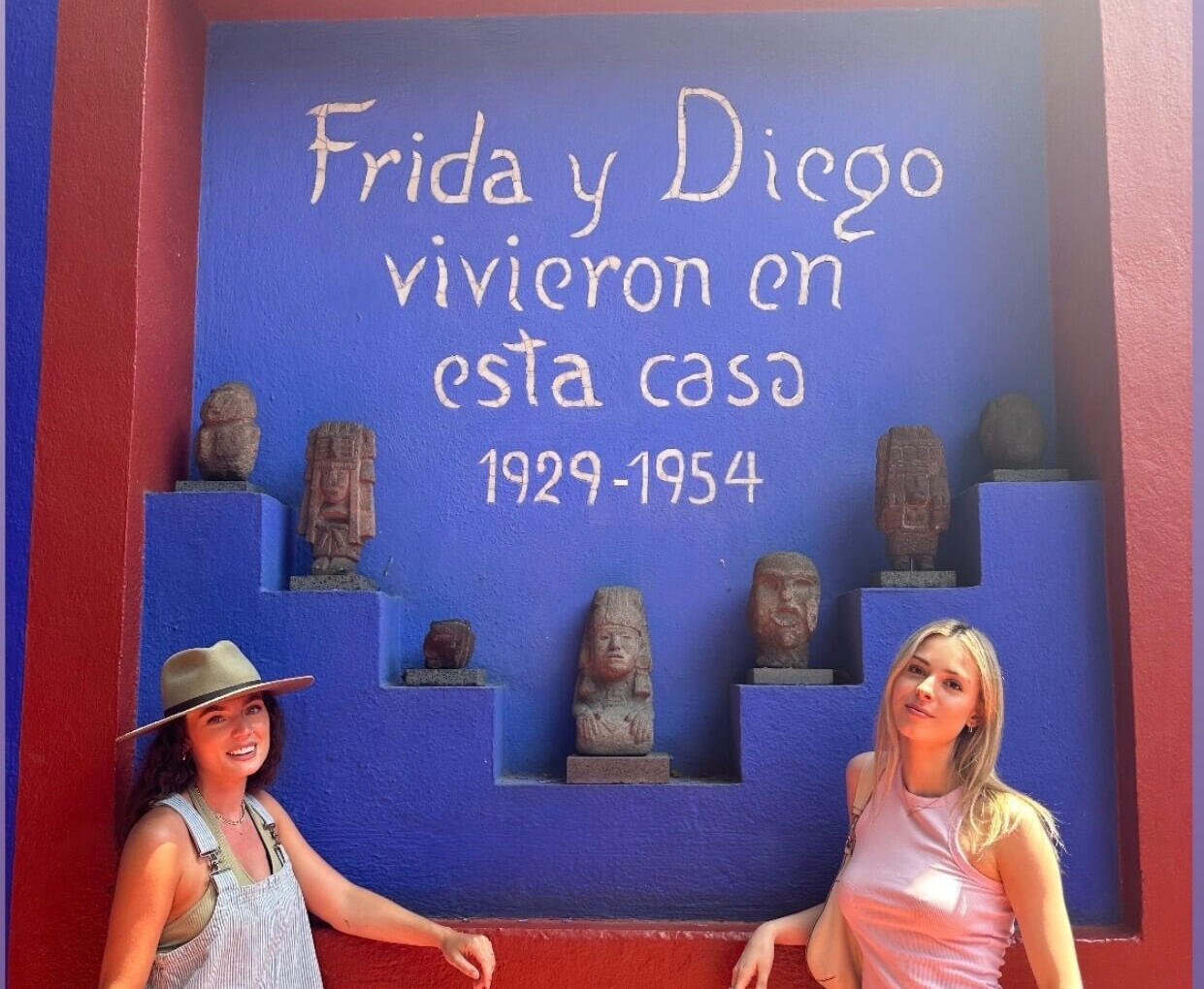 Two visitors posing in front of the famous 'Frida y Diego' mural at the Casa Azul in Coyoacán, highlighting the artistic and historical depth of our curated Mexico City tours.