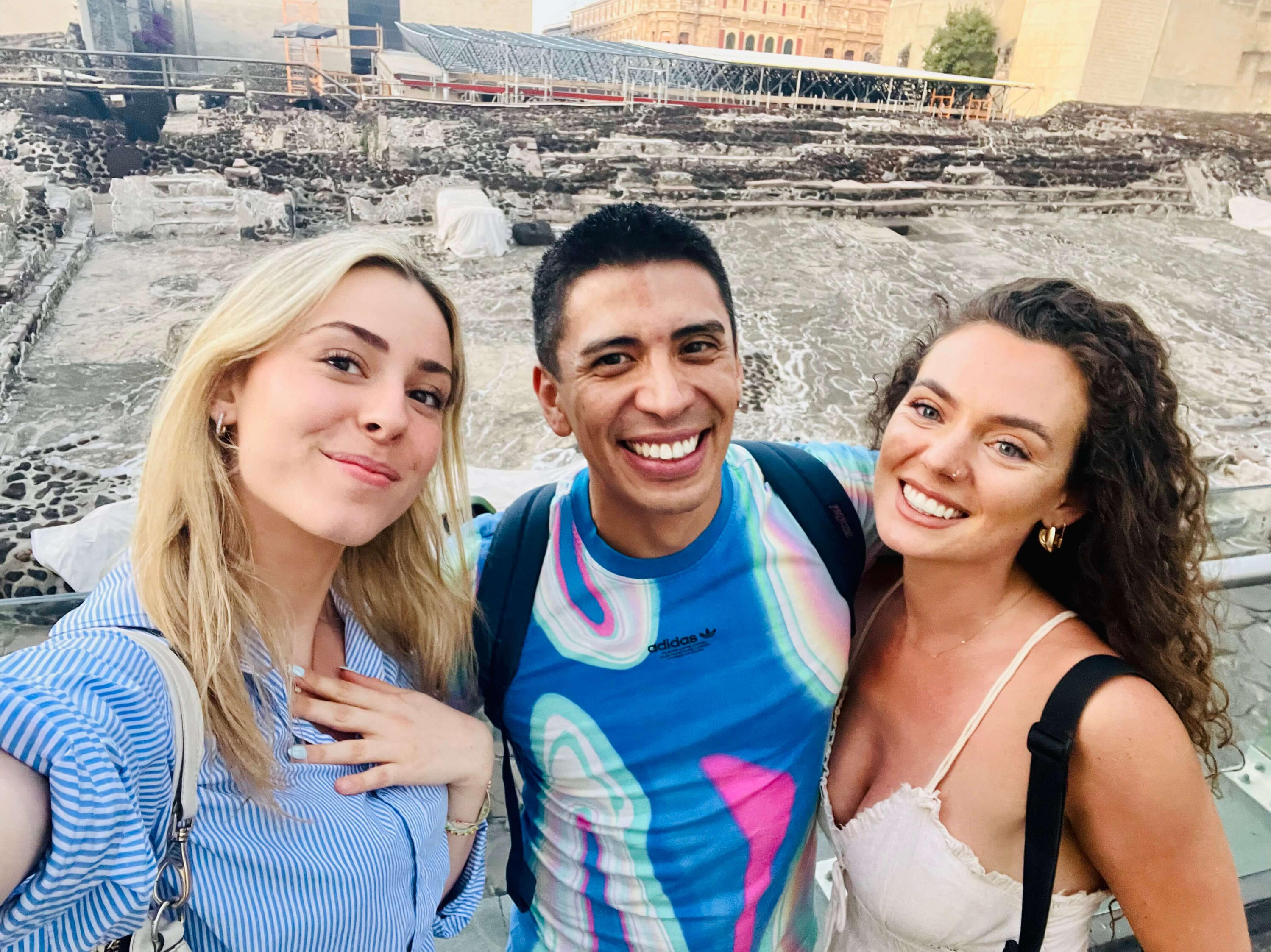 A joyful group selfie of Erik and two smiling guests at the ancient Templo Mayor ruins in Mexico City