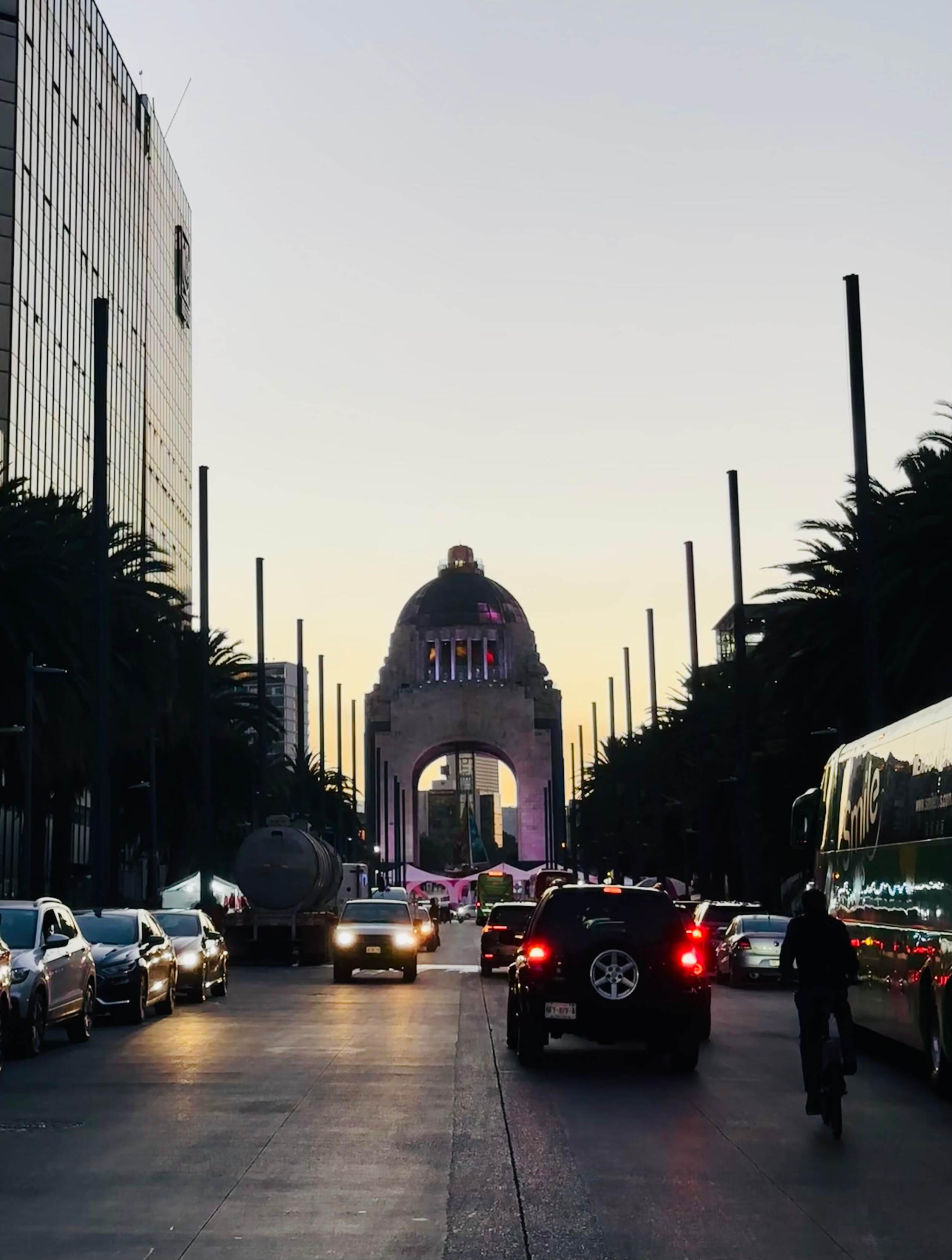 View of the illuminated Monument to the Revolution at sunset from a Mexico City street during a cultural walking experience.